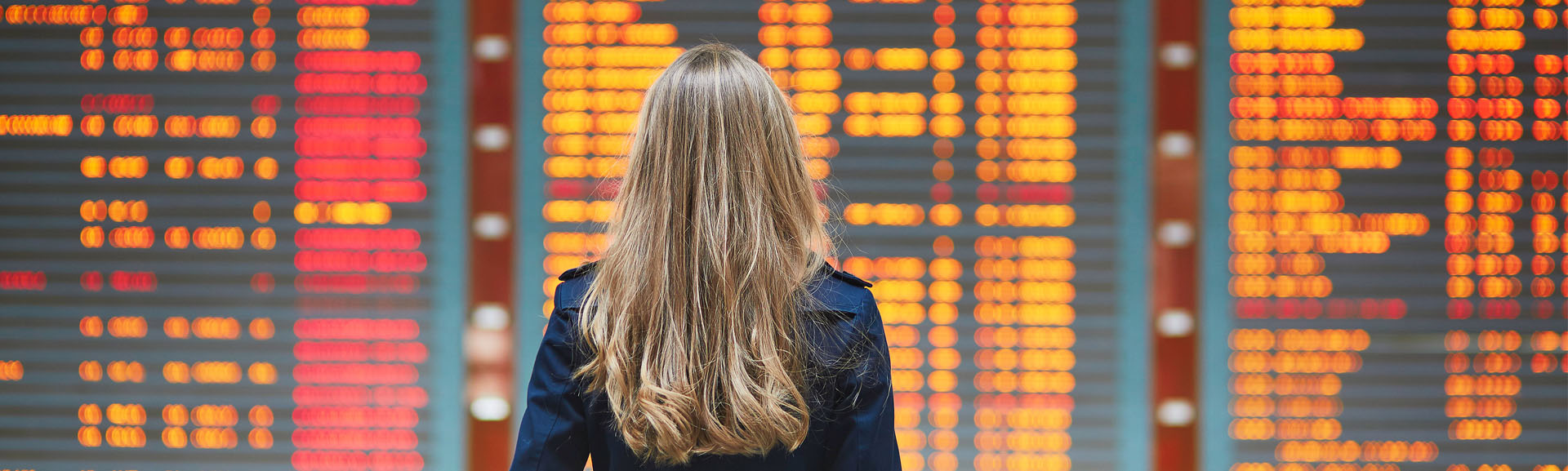 Woman looking at electronic departure board for canceled flight info