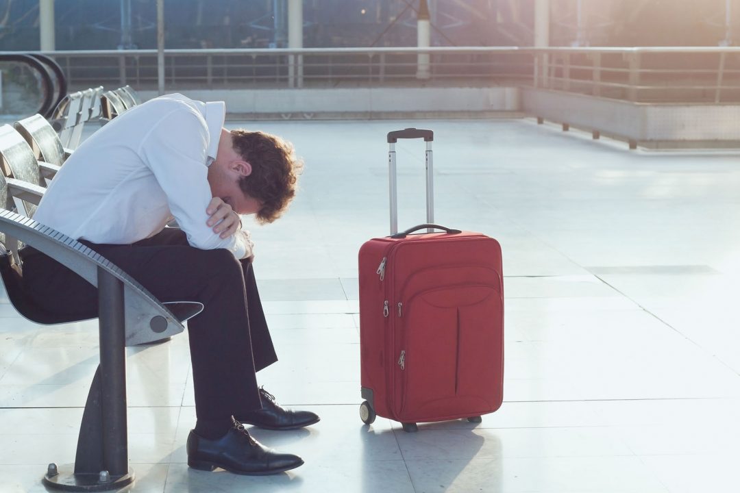 Well-dressed man sitting hunched over with red suitcase nearby