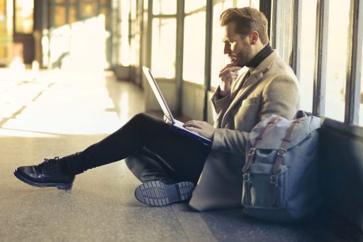 Young man sitting on airport floor, looking at laptop computer.