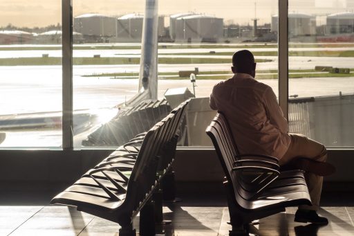 Man looking through window of airport at delayed aircraft by the gate