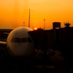 Delayed aircraft parked at gate with orange sky and sun setting in the background