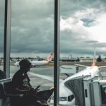 Person sitting at airport window with delayed flight in the background