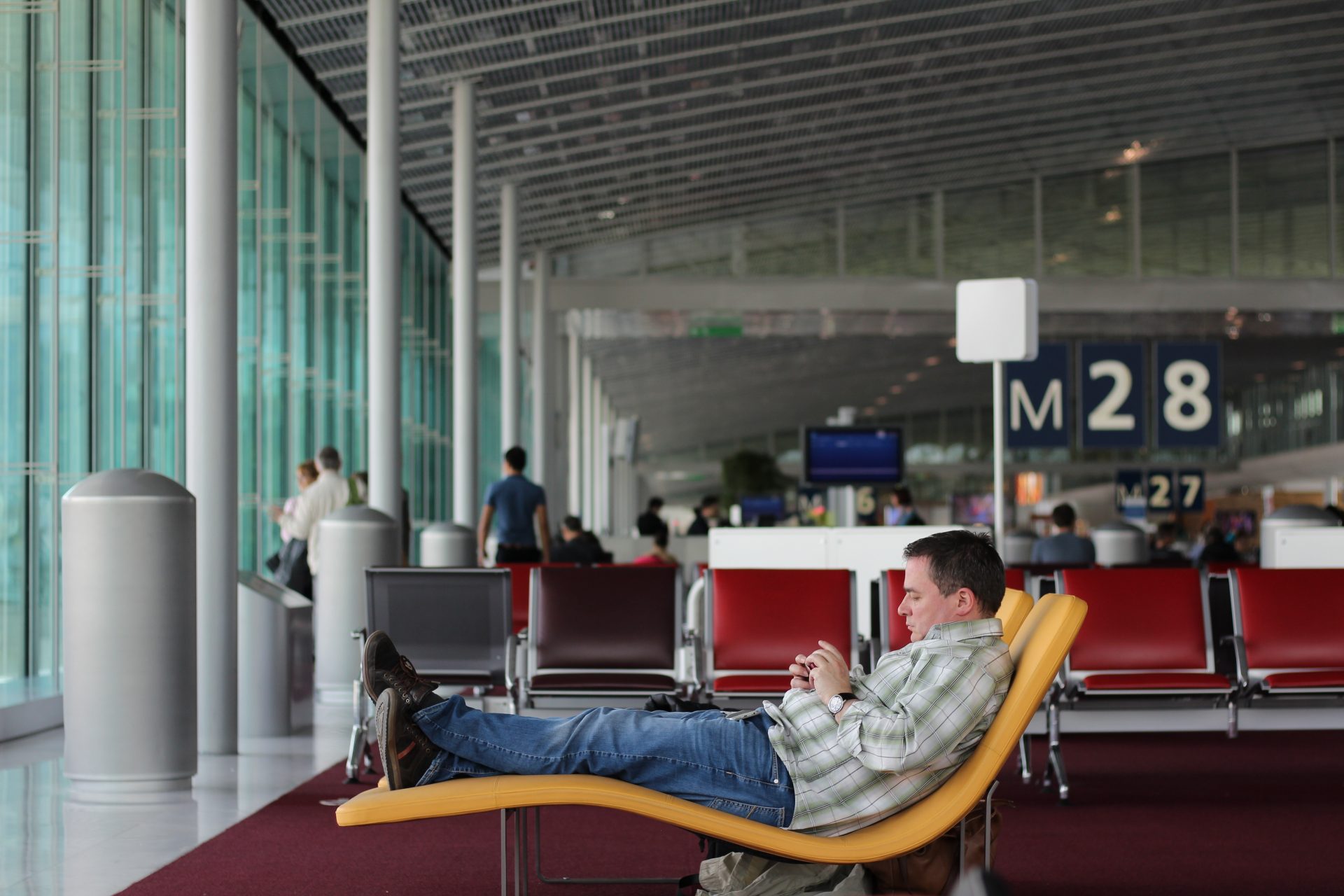 Man reclining at airport waiting area, checking phone for flight delays
