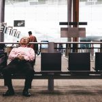 Older man sleeping at airport check in area, waiting for delayed flight