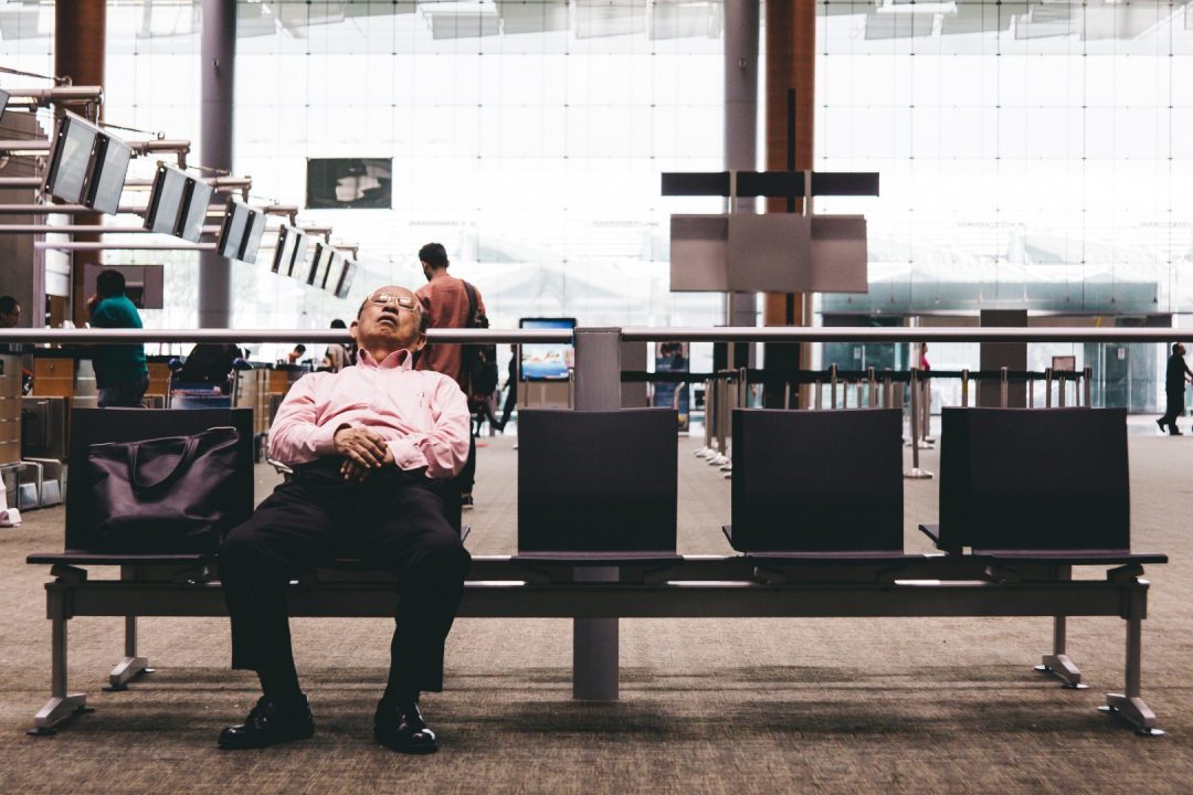 Older man sleeping at airport check in area, waiting for delayed flight