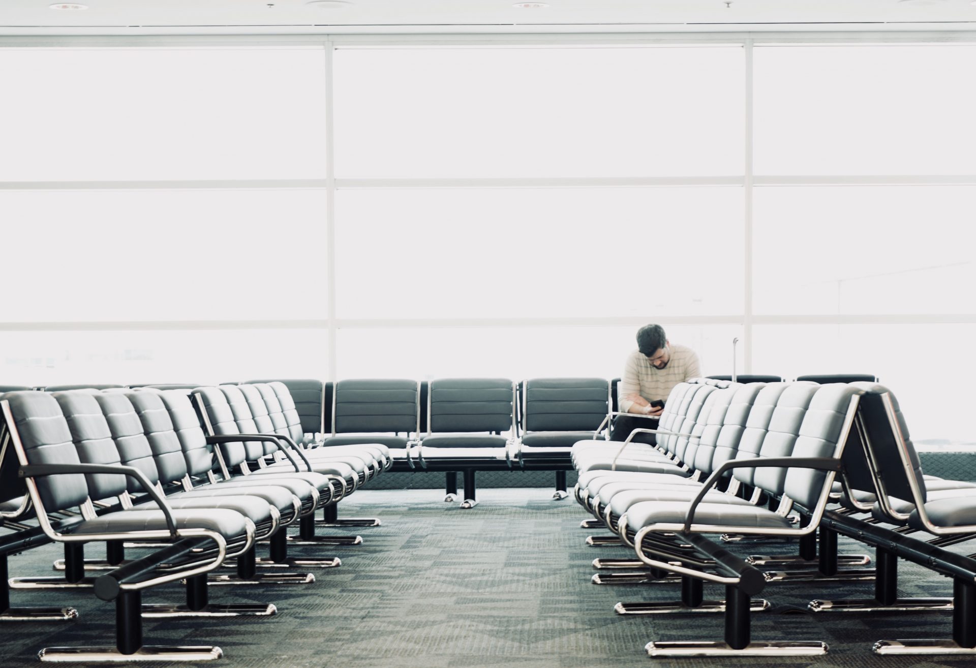 Man sitting alone at airport waiting area, checking phone for flight info
