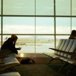 Sitting silhouettes against airport window, once checking phone for delayed flight info